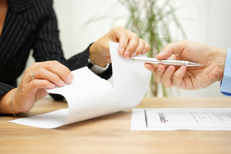 Person tearing up a severance agreement while another person offers a pen across an office desk.